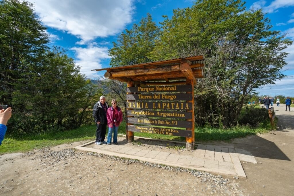 Pareja posando junto al cartel de madera de Bahía Lapataia, en el Parque Nacional Tierra del Fuego, donde finaliza la Ruta Nacional 3