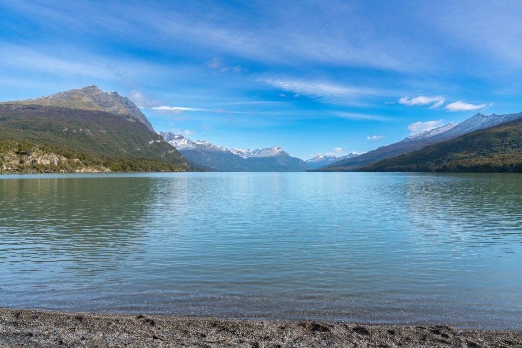 Lago de aguas turquesa y calmas rodeado de montañas con picos nevados y cielo azul en el Parque Nacional Tierra del Fuego