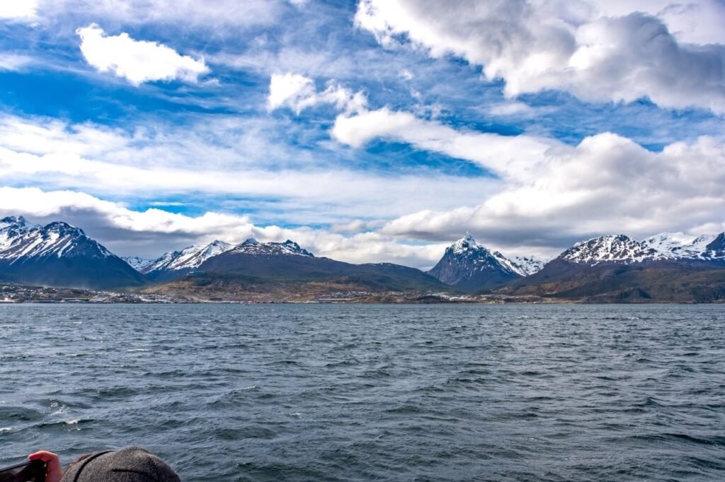 Vista de la ciudad de Ushuaia y las cumbres nevadas desde el Canal Beagle, con aguas agitadas y cielo con nubes