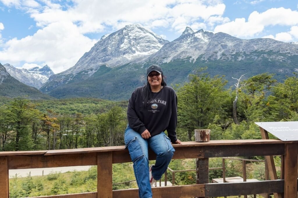 Turista sonriendo en el Mirador Cerro Cornú, con montañas nevadas y bosque de lengas al fondo, Tierra del Fuego
