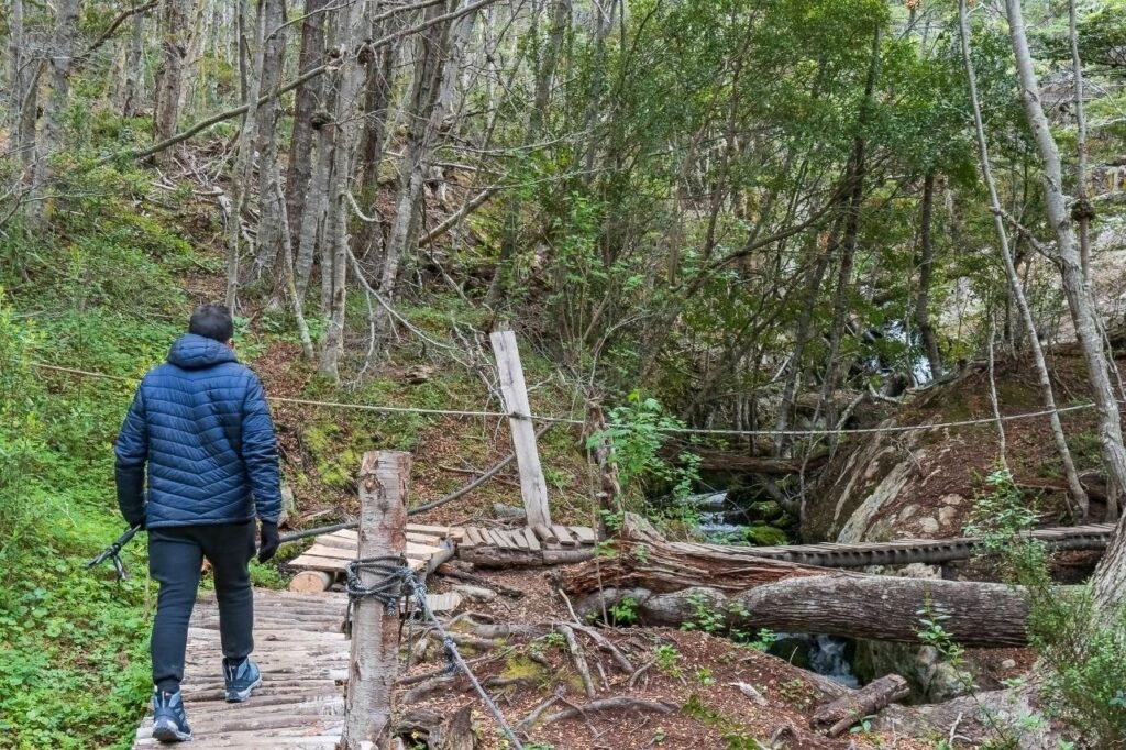 Excursionista cruzando una pasarela de madera en el bosque camino a la Cascada del Duende, Tierra del Fuego