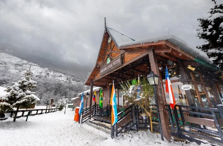 Fachada de madera de la Estación Principal del Tren del Fin del Mundo con banderas internacionales y nieve, Ushuaia.