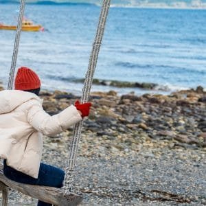 Turista disfrutando de una hamaca frente al Canal Beagle en Puerto Almanza, Tierra del Fuego, con botes pesqueros de fondo.