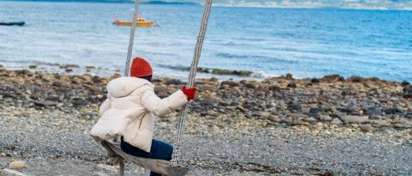 Turista disfrutando de una hamaca frente al Canal Beagle en Puerto Almanza, Tierra del Fuego, con botes pesqueros de fondo.