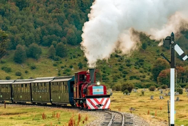 La locomotora de vapor roja y negra del Tren del Fin del Mundo arrastra vagones en medio de bosques y montañas en Ushuaia, Argentina.