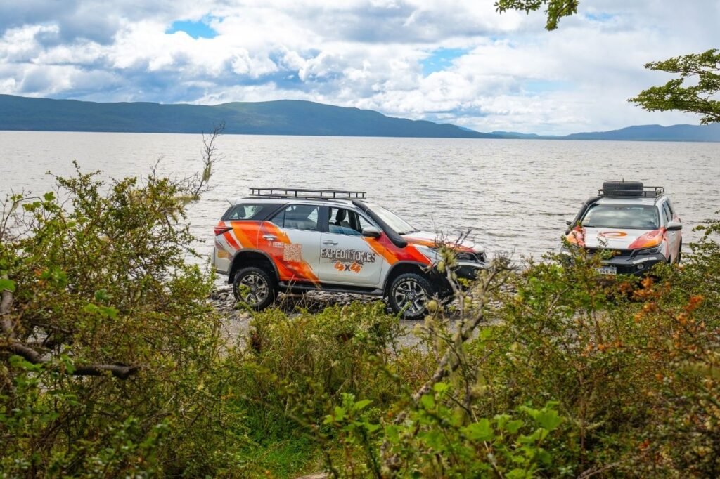 Dos camionetas 4x4 de Expediciones 4x4 estacionadas en la costa del Lago Fagnano con pedregullo y montañas al fondo, en Tierra del Fuego.
