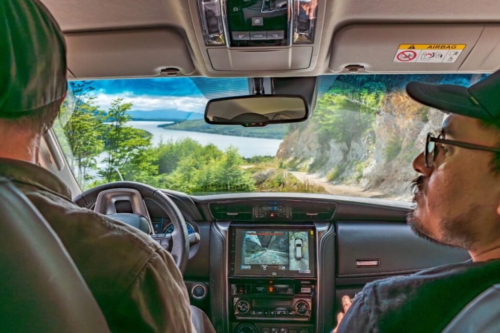 Vista desde el interior de una camioneta 4x4 del lago Escondido, entre montañas y bosque. Con un camino de montaña junto a la ladera rocosa en Tierra del Fuego.