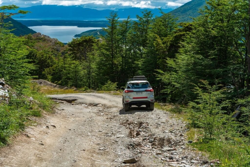 Camioneta 4x4 bajando por el antiguo paso de la ruta 3, un camino de ripio con piedras entre bosque de lengas y montañas al fondo en Tierra del Fuego.
