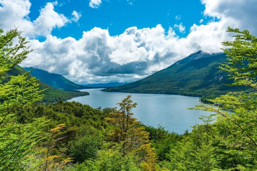 Vista panorámica del lago Escondido, rodeado de montañas cubiertas de bosque y nubes bajo cielo azul en Tierra del Fuego.