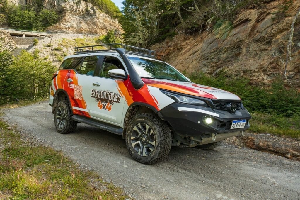 Camioneta Toyota 4x4 de Expediciones 4x4 con parrilla y snorkel sobre un camino de ripio junto a paredes de roca y bosque en Tierra del Fuego.