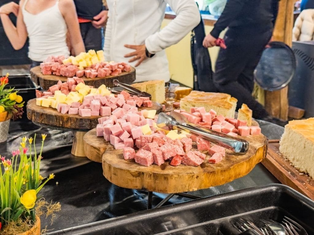 Tablas de madera con variedad de fiambres, quesos picados en cubos y panes caseros en el buffet de Park Austral.