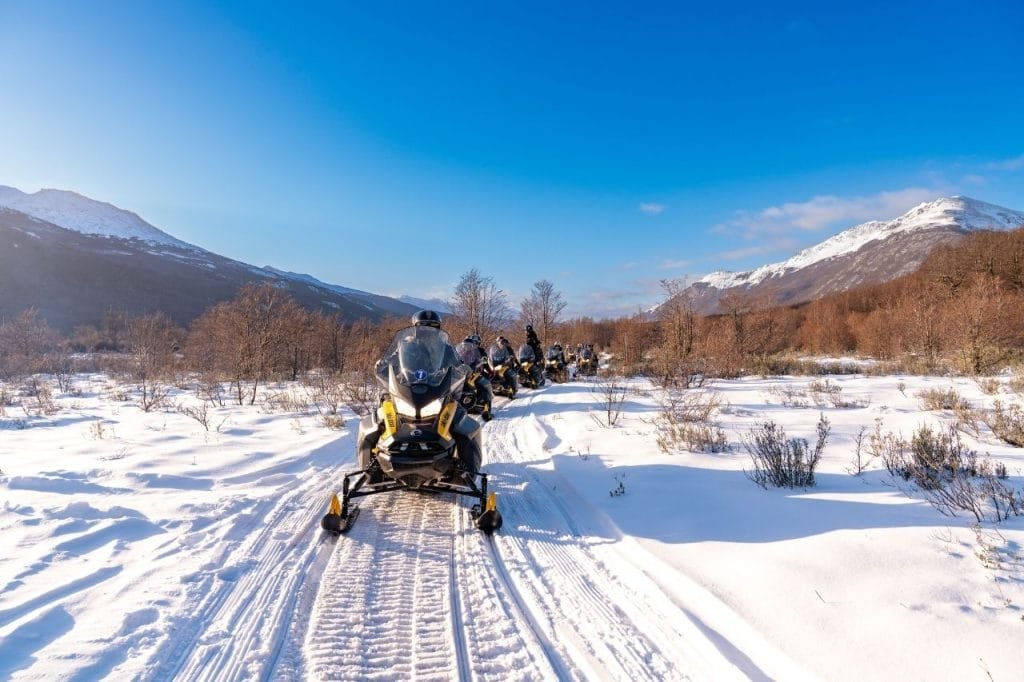 Caravana de motos de nieve avanzando de frente por un camino nevado en Park Austral, Ushuaia.