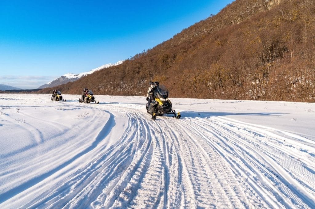 Motos de nieve recorriendo un sendero marcado en la nieve sobre la ladera de una montaña en Park Austral.