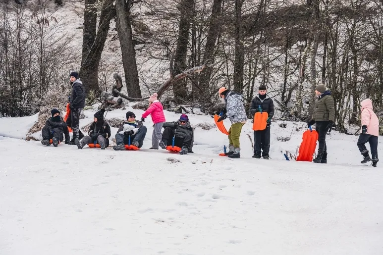 Grupo familiar divirtiéndose con sliders naranjas en la nieve en Ushuaia.