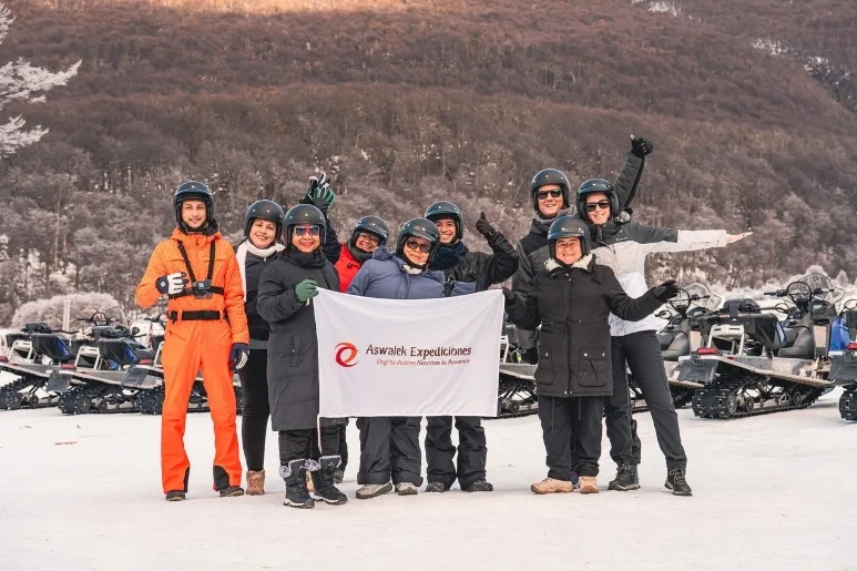 Grupo de turistas con cascos y bandera de Aswalek Expediciones en la nieve de Ushuaia.