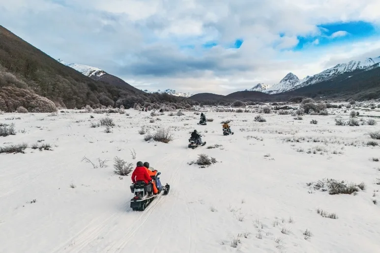 Grupo en motos de nieve recorriendo valle nevado en Ushuaia. Excursión de invierno.