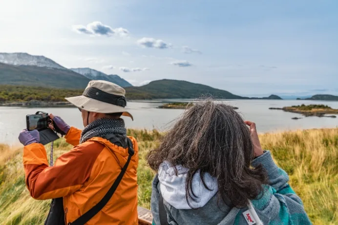 Turistas tomando fotos con sus celulares de la Bahía Lapataia y las montañas nevadas en el Parque Nacional Tierra del Fuego, Ushuaia.