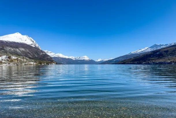 Vistas panorámicas del lago Roca y montañas nevadas en el Parque Nacional Tierra del Fuego, cerca de Ushuaia, bajo un cielo azul despejado.