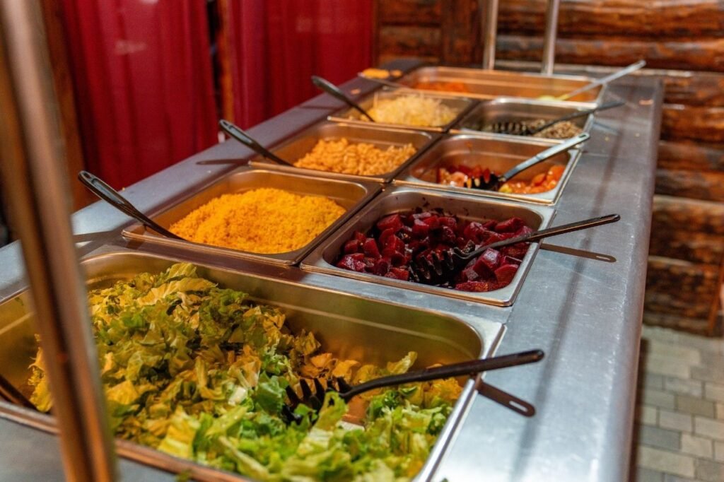 Barra de buffet self-service en acero inoxidable con variedad de ensaladas frescas, lechuga, remolacha y aderezos.