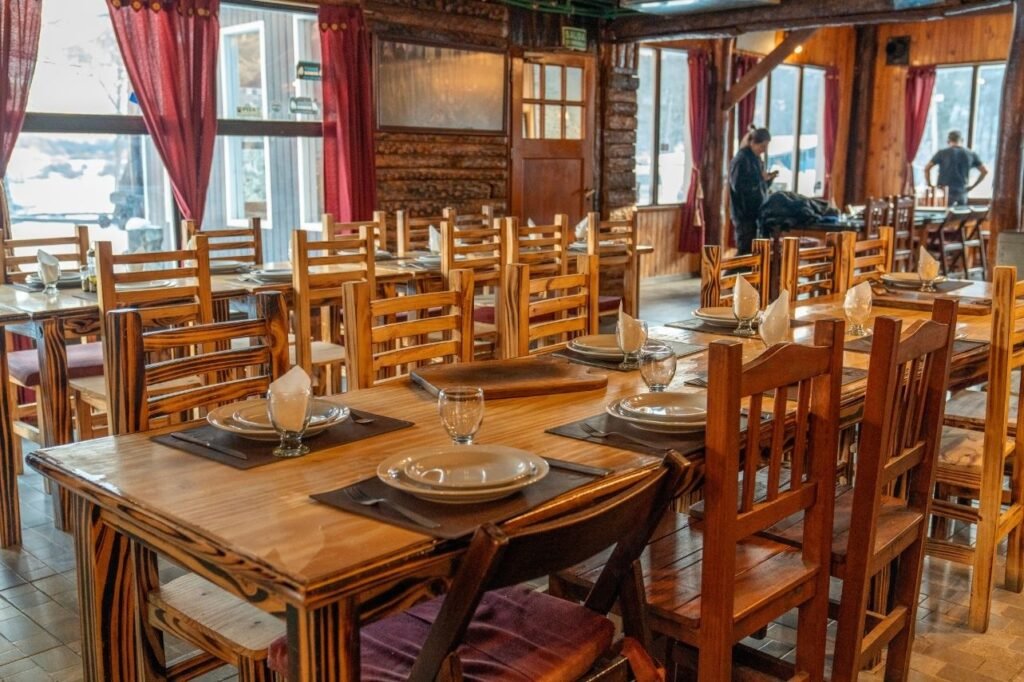 Salon comedor con mesas y sillas de madera rústica armadas para almorzar en el Centro Invernal Las Cotorras.