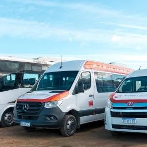 Flota de vehículos de transporte de la agencia Aswalek en Ushuaia, que incluye un minibús Agrale, un furgón Mercedes-Benz Sprinter y una minivan Toyota Hiace, estacionados frente a montañas nevadas.