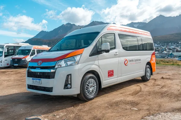 Camioneta Toyota Hiace, estacionada en un camino de tierra con montañas nevadas y la ciudad de Ushuaia al fondo bajo un cielo nublado.