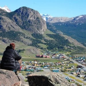 Turista sentado en una roca contemplando el pueblo de El Chaltén y las montañas.