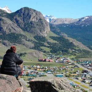 Turista sentado en una roca contemplando el pueblo de El Chaltén y las montañas.
