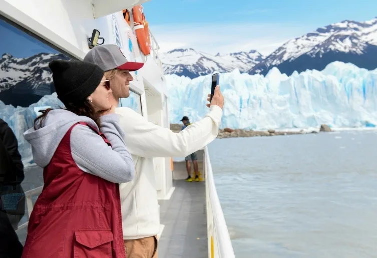 Pareja sacando una selfie en la cubierta de un barco frente al glaciar Perito Moreno.