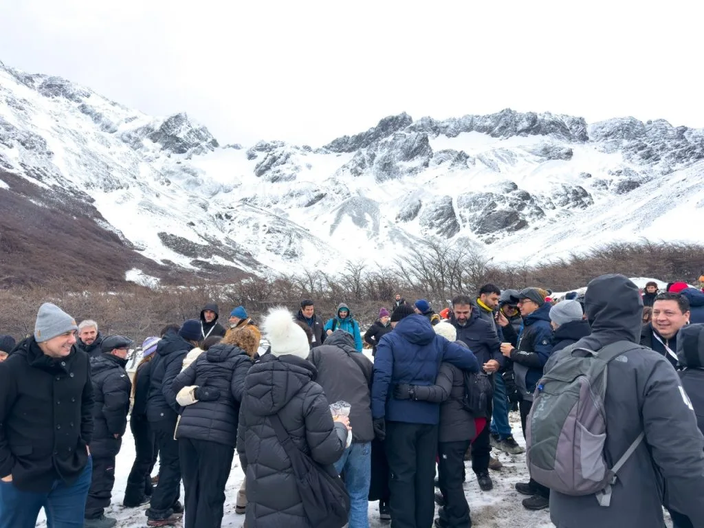 Un grupo de turistas con ropa de invierno de pie en la nieve al pie del Glaciar Martial, con imponentes montañas andinas nevadas al fondo, Ushuaia.
